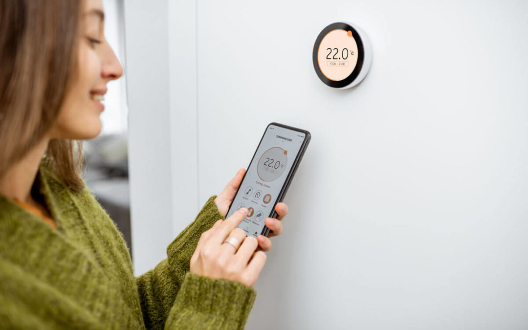 Woman dressed in green sweater regulating heating temperature with a modern wireless thermostat and smart phone at home