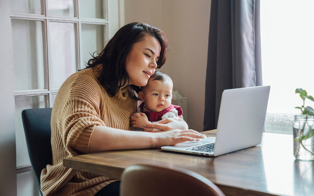 Mom holding baby and working from home on laptop